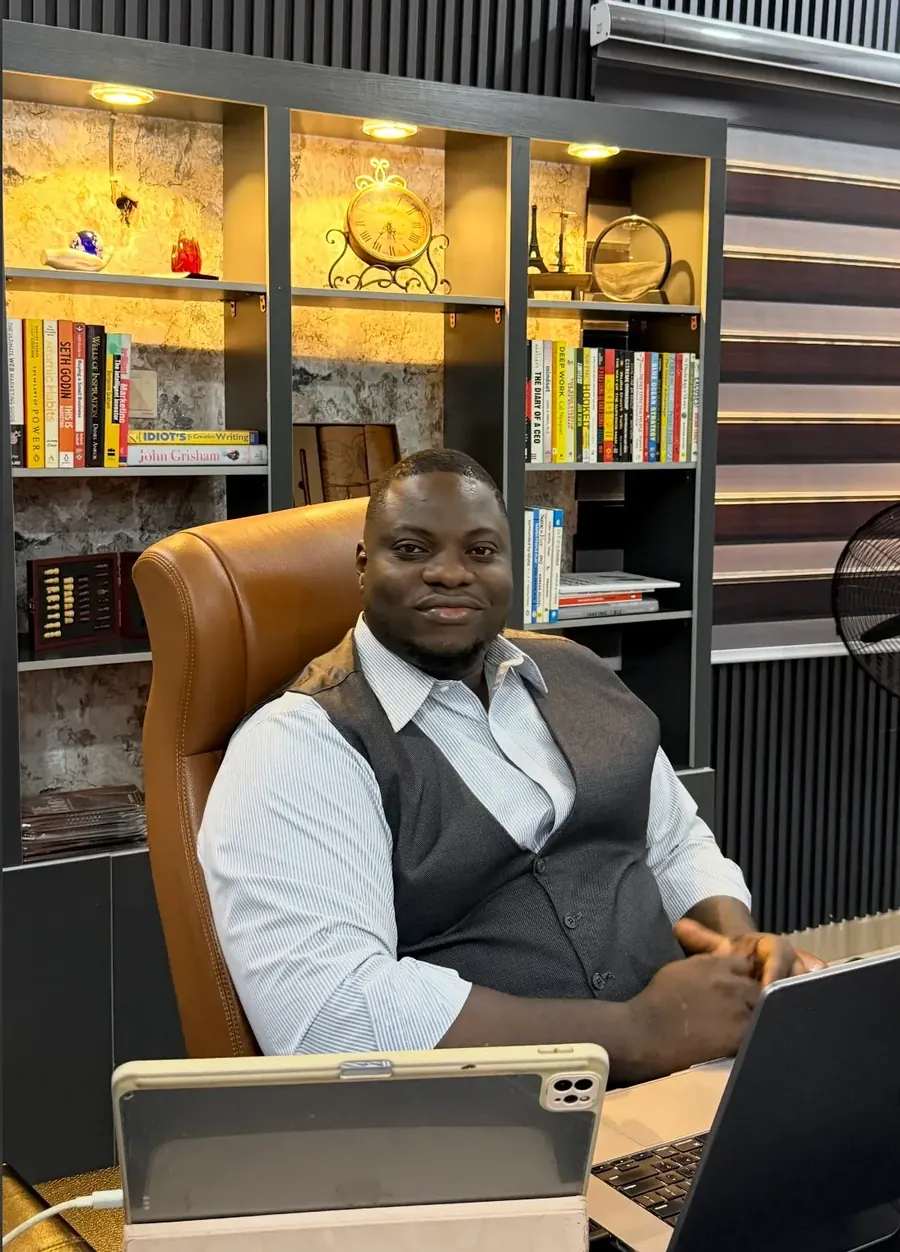 Fredrick Eghosa at his desk in his Lagos office, in front of a lit bookshelf